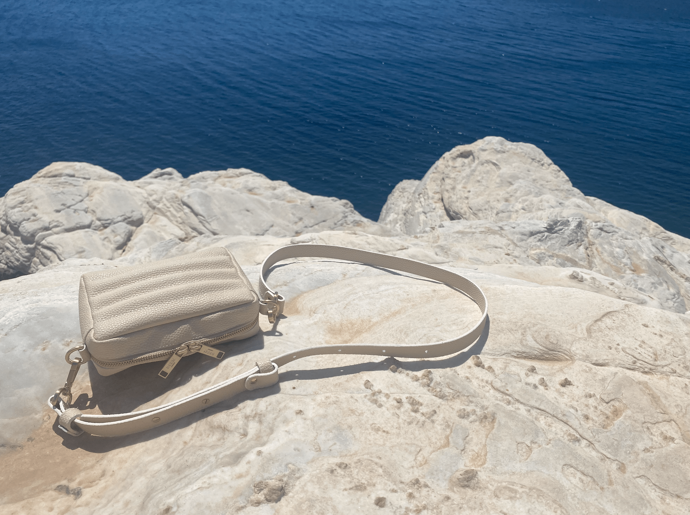 Ridley Crossbody in Oat on rocks near the ocean